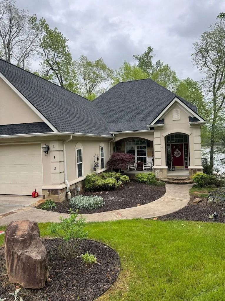A beige house with a dark shingle roof, a two-car garage, and a curved stone walkway leading to a red front door.