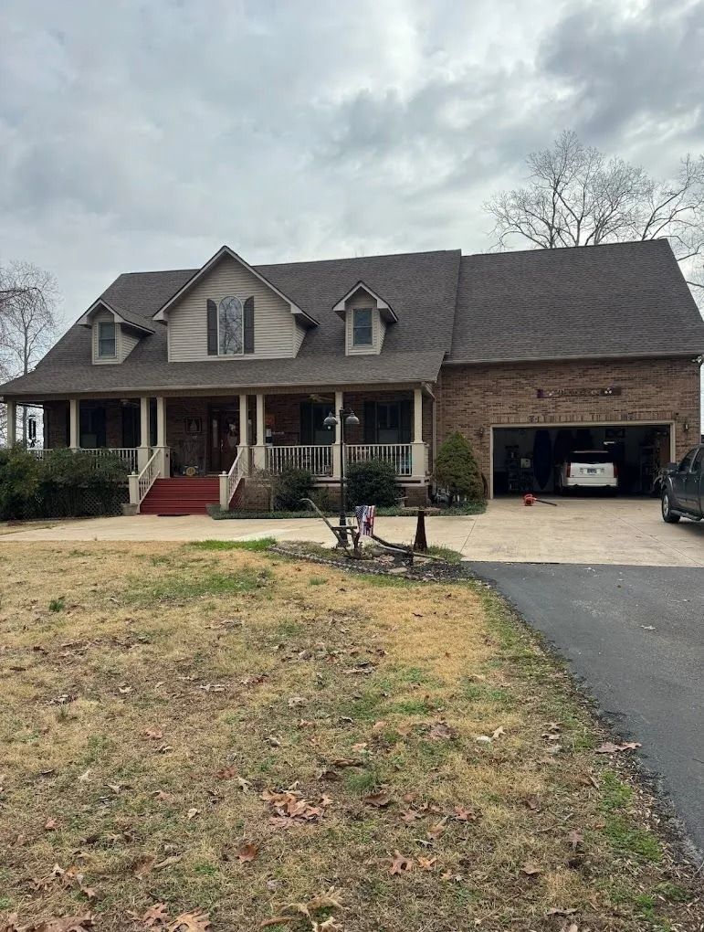 A two-story brick and siding house with a front porch, dormer windows, and an attached two-car garage.