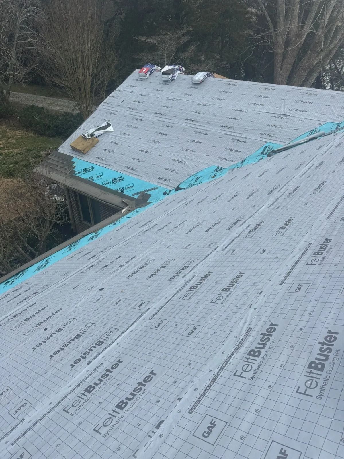 A high-angle view of a residential roof undergoing renovation, covered in grey FeltBuster underlayment and blue flashing.