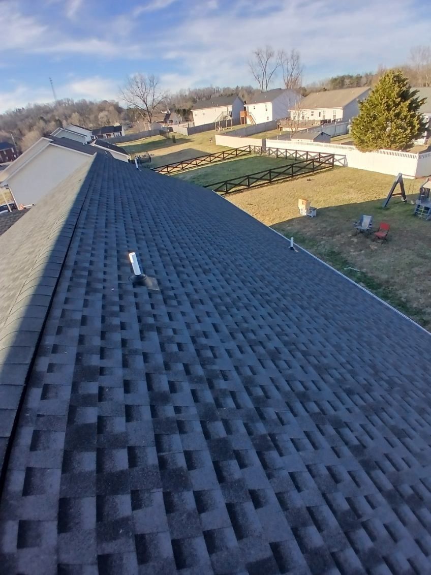 A high-angle view of a newly shingled gray roof overlooking a suburban backyard on a sunny day.