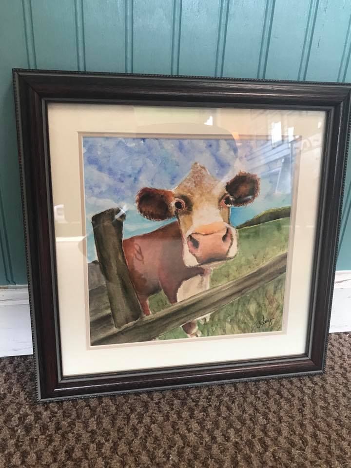 A framed painting of a cow peeking over a fence.