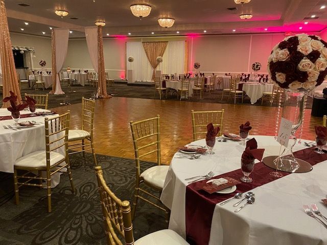 Banquet hall set for a wedding with round tables, gold chairs, and burgundy accents.