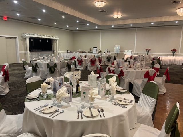 Formal event hall with round tables set for a meal, decorated with white, green, and red accents.