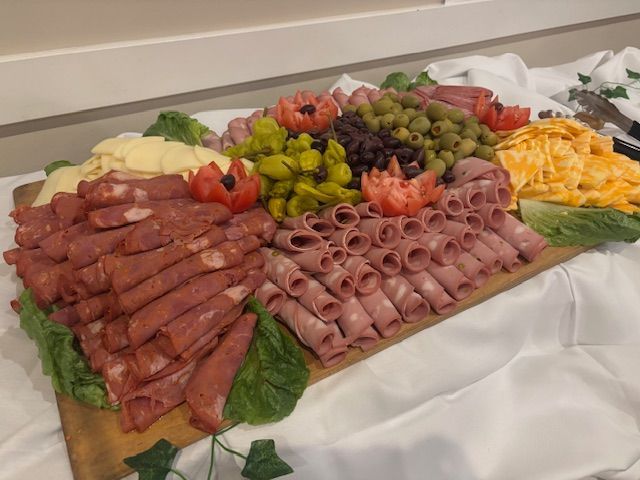Charcuterie board with meats, cheeses, olives, and peppers arranged on a wooden platter with garnishes.