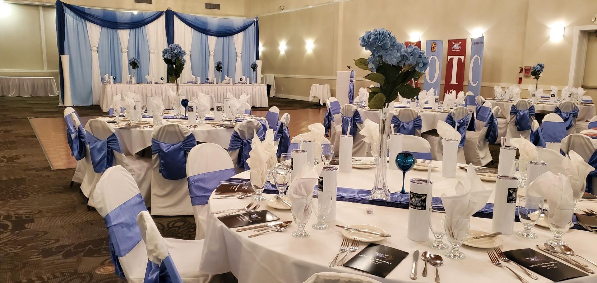 A decorated reception hall in blue and white with tables, chairs, and a head table.