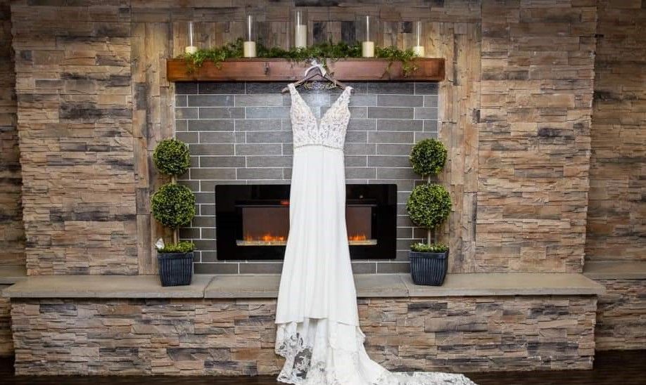 Wedding dress hanging on a hanger in front of a fireplace with candles and plants.