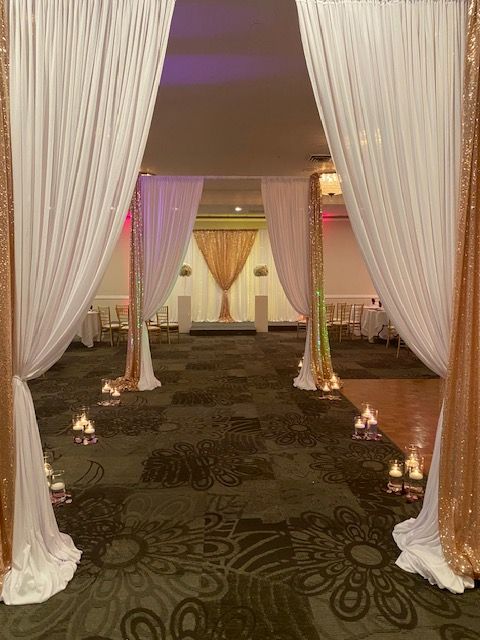 Elegant event entrance with white and gold draped fabric and candles.