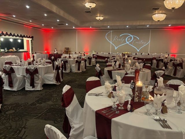 Wedding reception hall with round tables set for guests, decorated in white and burgundy.  
