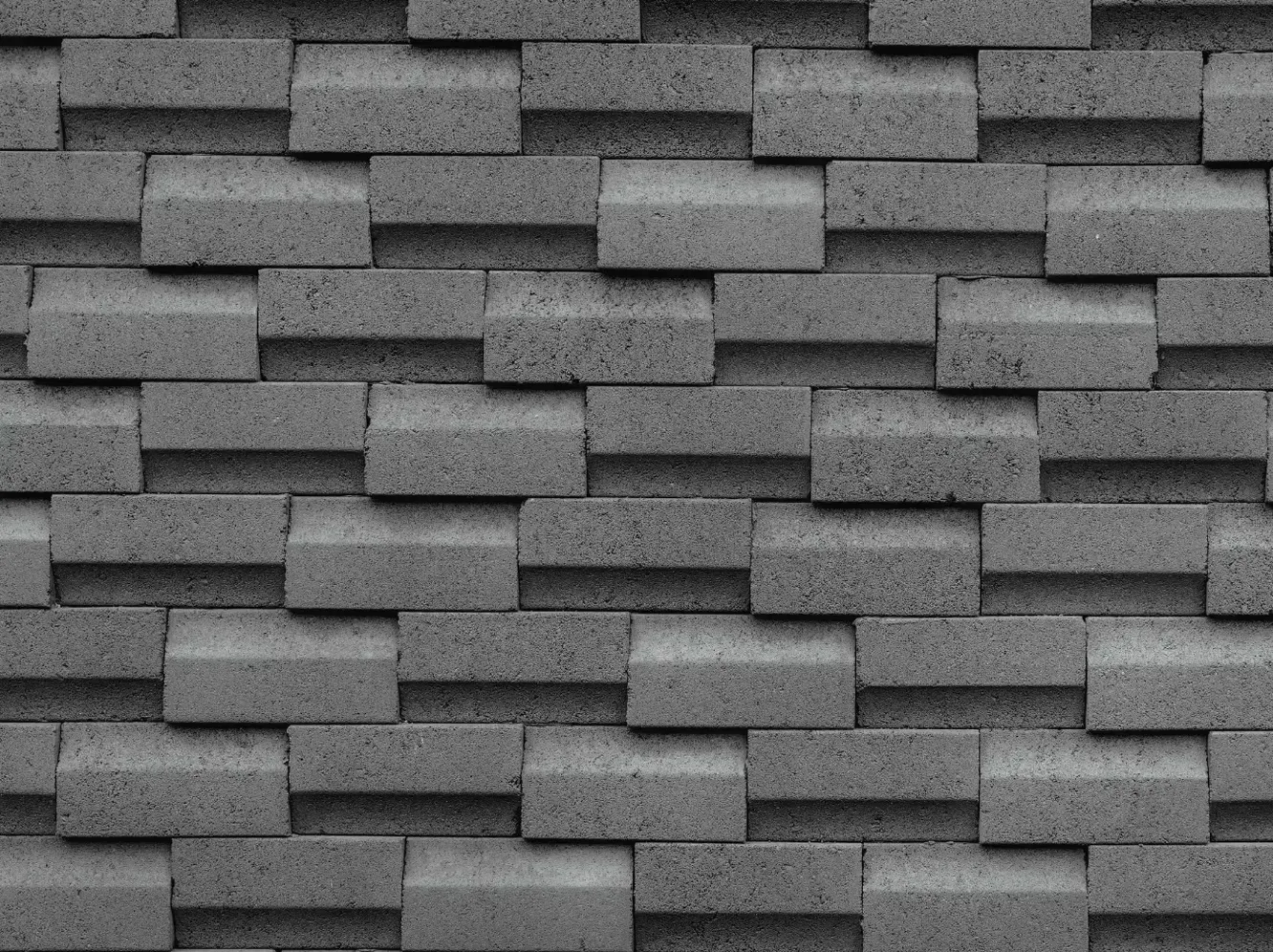 A gray wall featuring a textured, staggered pattern of rectangular stone bricks with alternating depths.