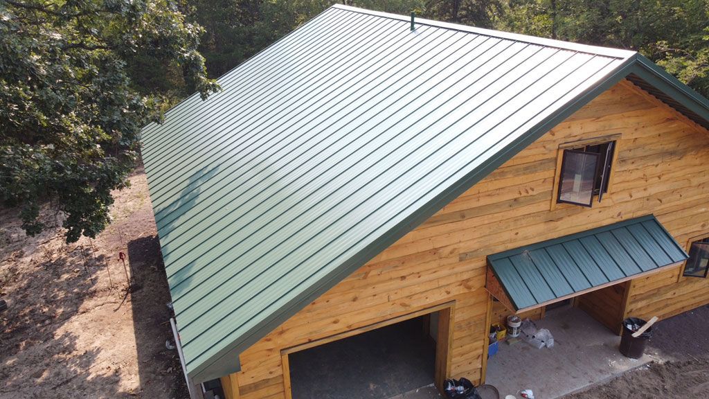 An elevated view of a wooden cabin with a green metal roof, featuring a garage door and a covered side entrance.