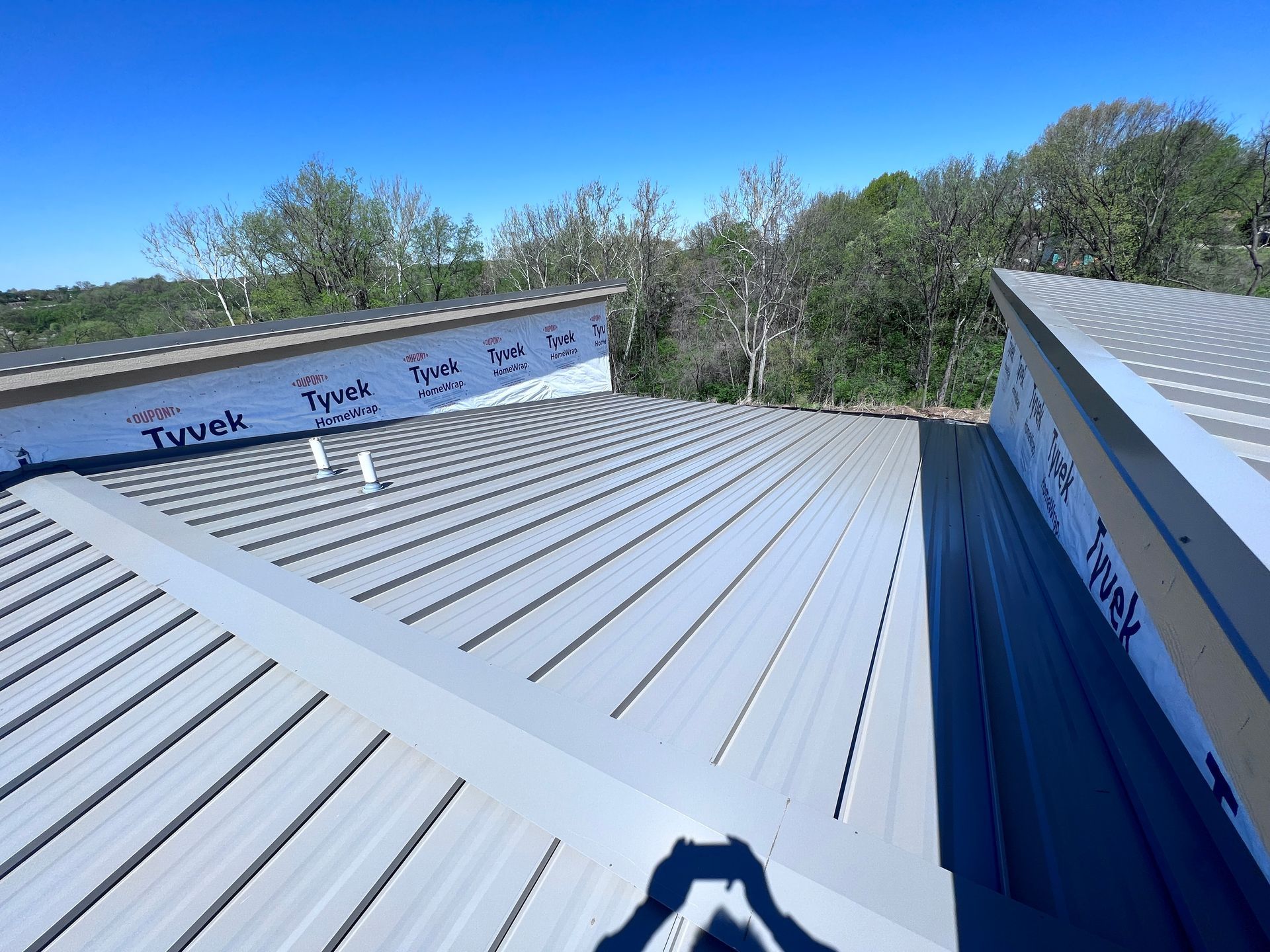 An elevated view of a metal roof under construction with Tyvek house wrap visible on the upper wall sections.