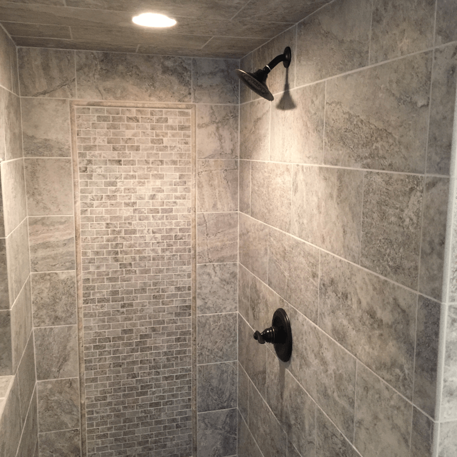 A shower with gray tiles and a black shower head
