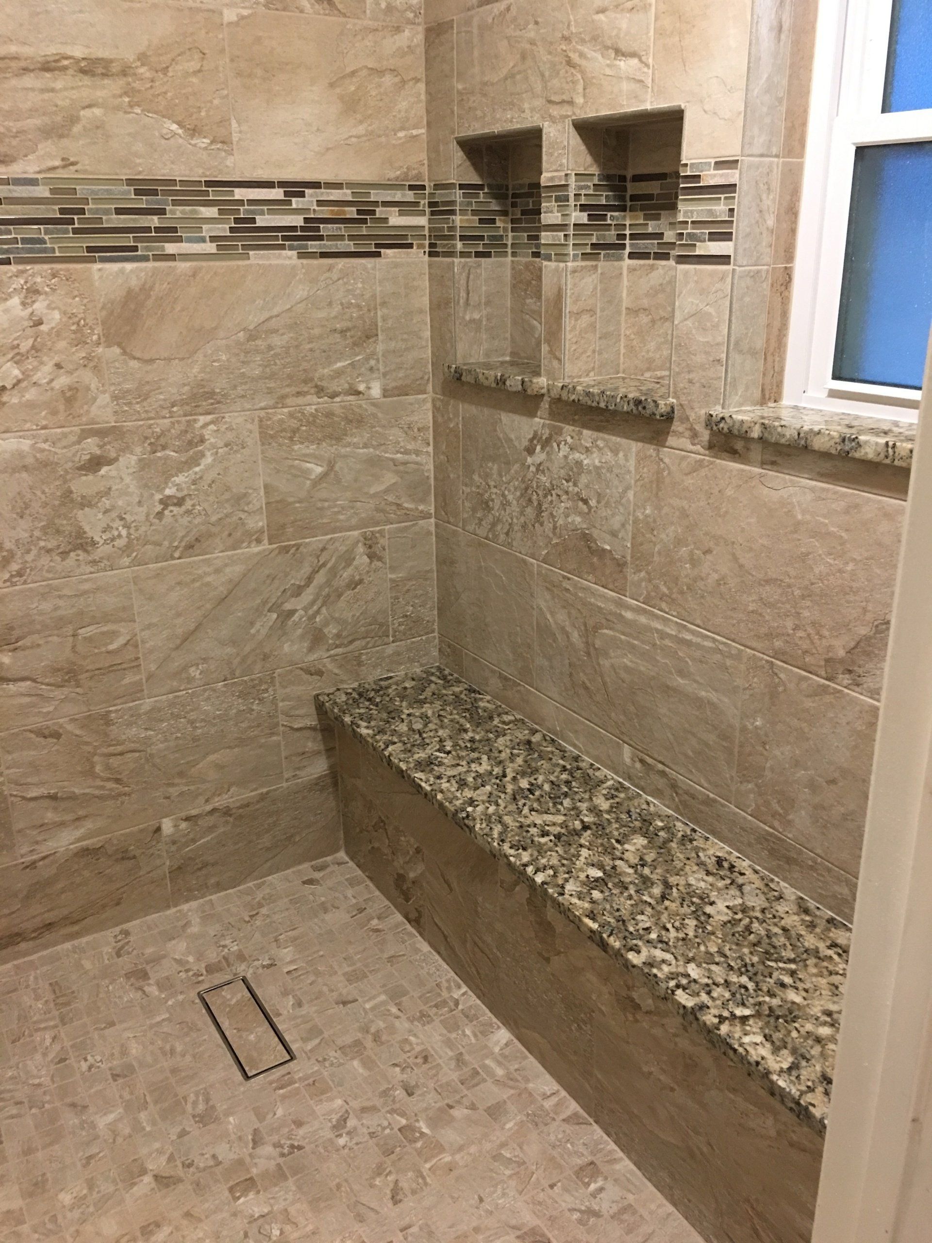 A bathroom with a walk in shower with a bench and a window.