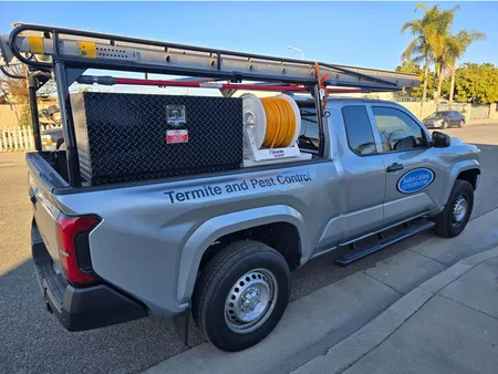 Silver pest control truck parked on a street. Toolbox and equipment in the truck bed.