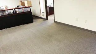 Empty office with gray carpet, white walls, and a dark counter.