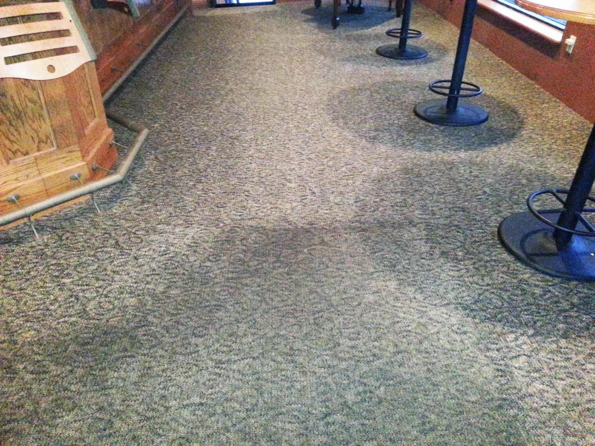 Close-up of dirty, textured carpet in a bar area with table legs.