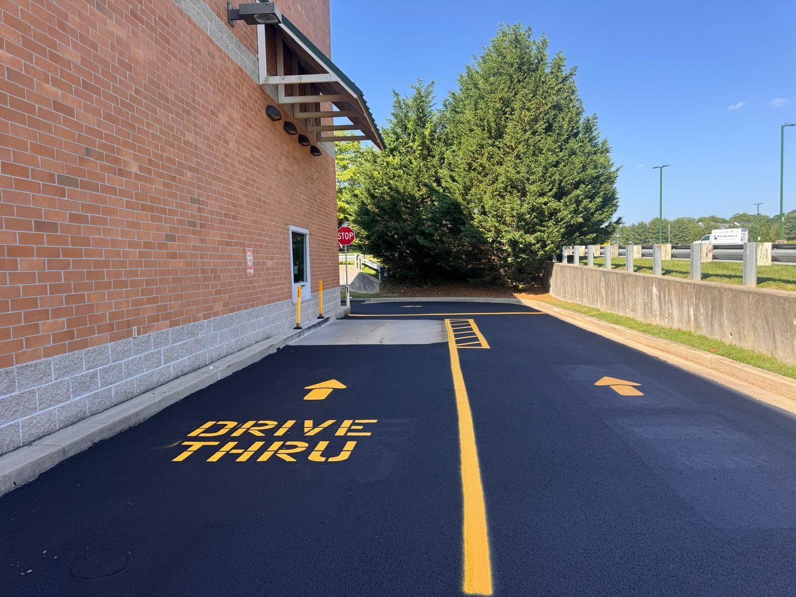 Drive-thru lane beside a brick building, with painted arrows and yellow “DRIVE THRU” text on the pavement.