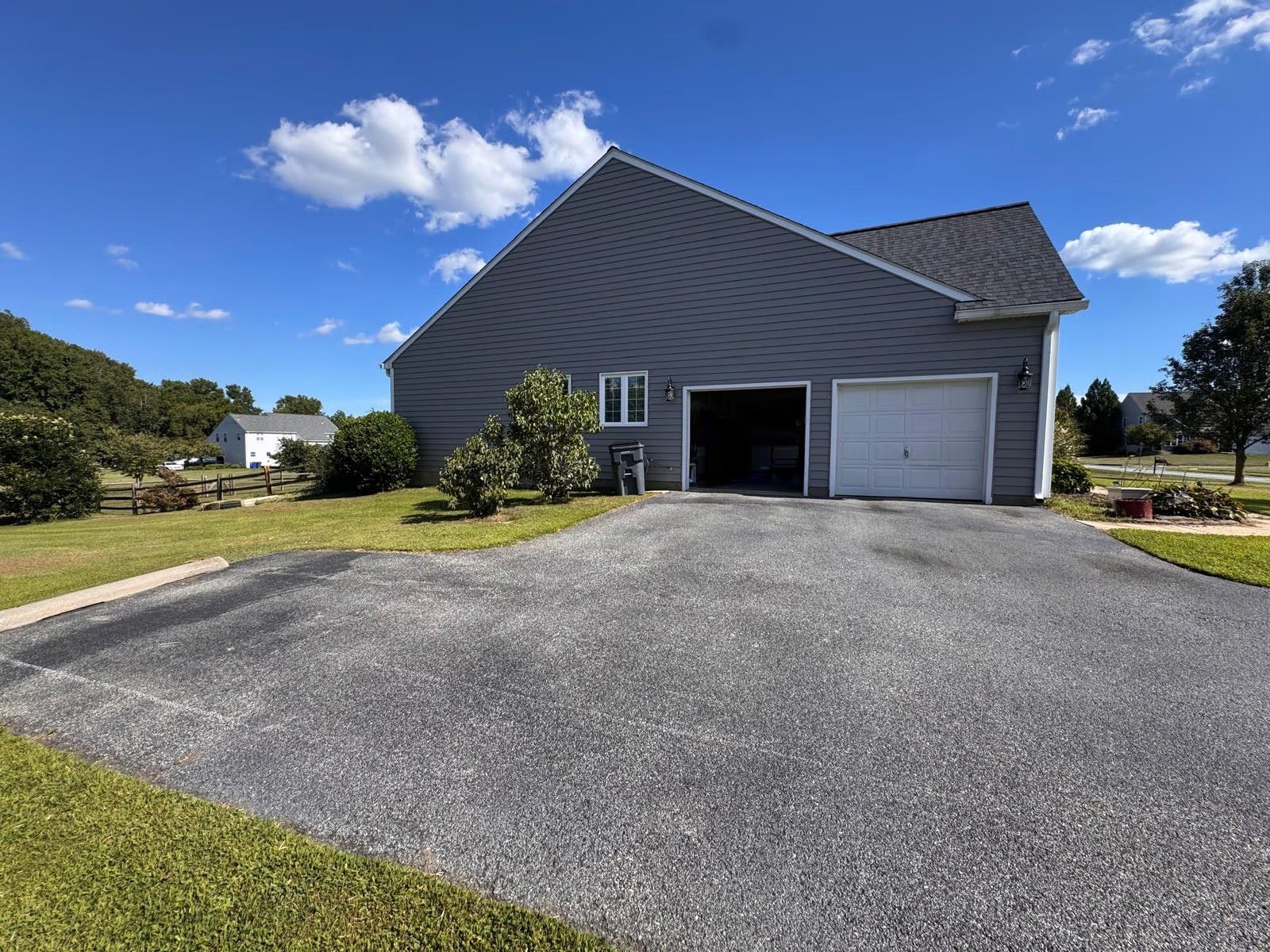 Gray house with two garage doors and a wide gravel driveway under a blue sky
