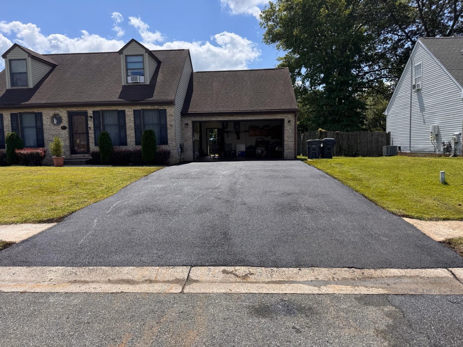 Suburban house with a newly paved black driveway and attached garage under a blue sky