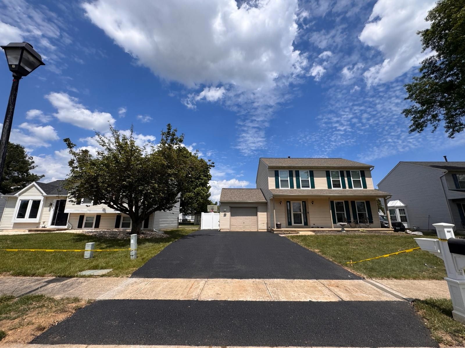 Suburban house with black driveway, white garage, and partly cloudy blue sky