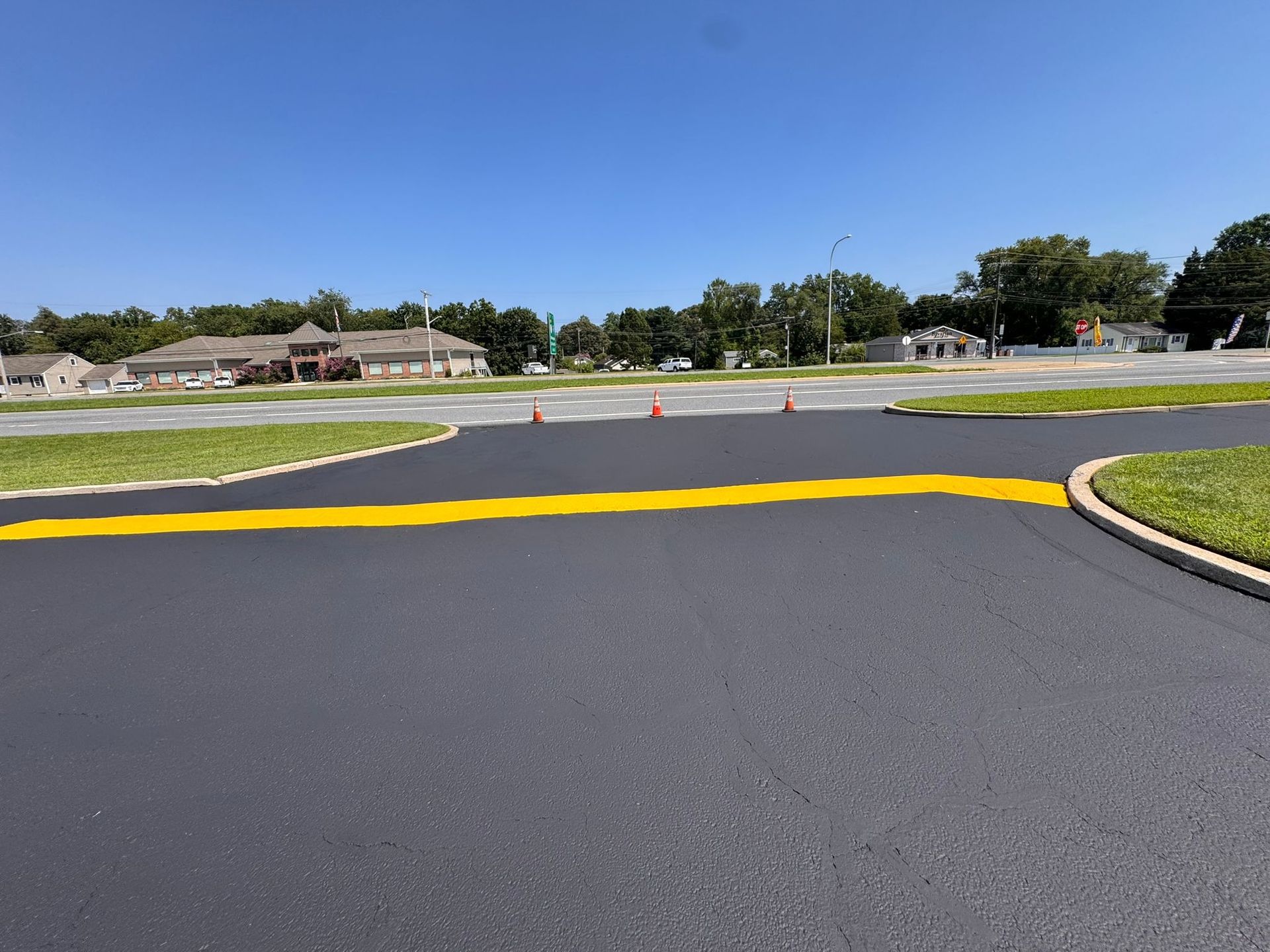 Empty paved road with a yellow speed bump, grassy median, and houses under a clear blue sky.
