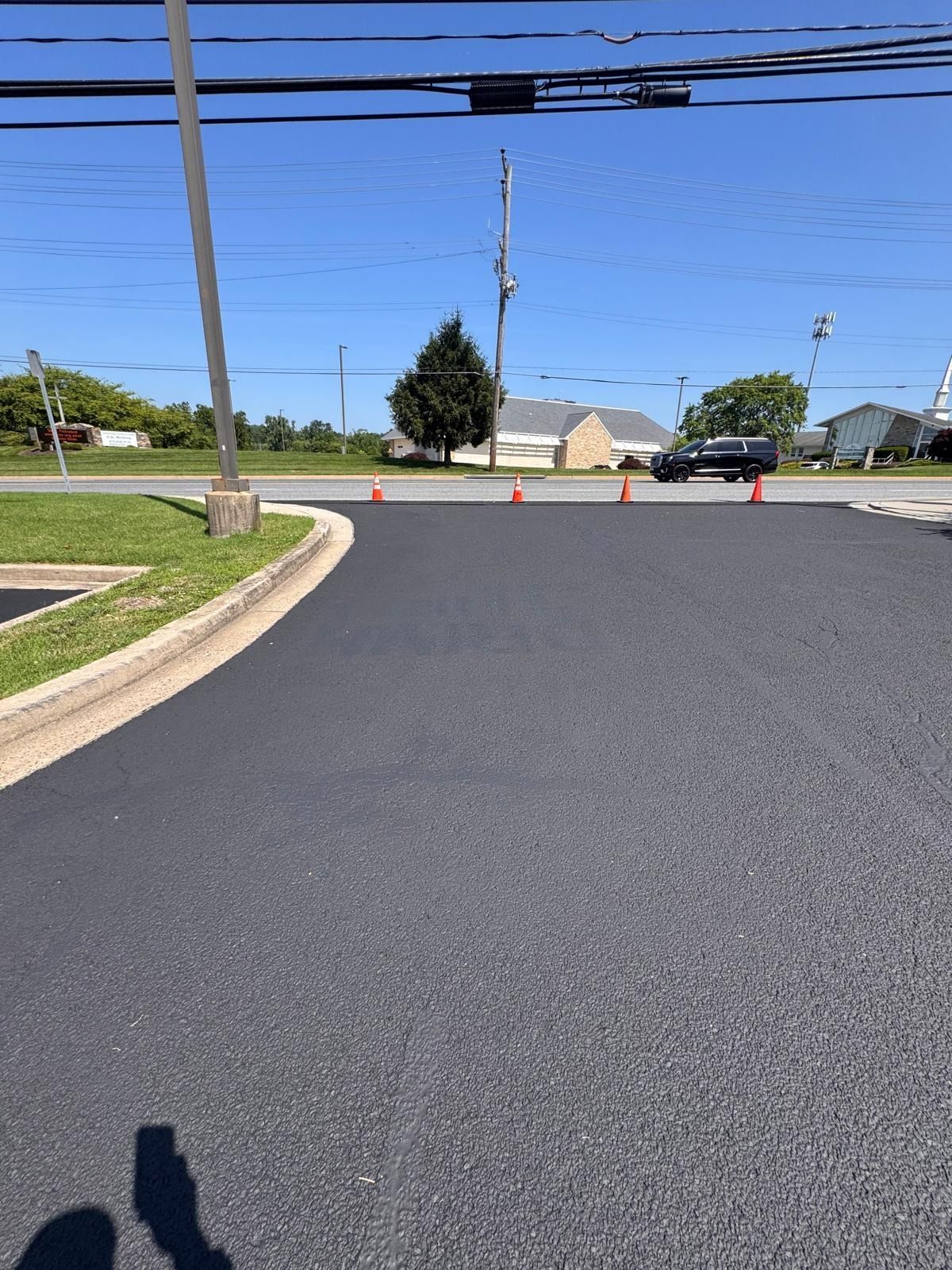 Freshly paved road with orange cones, utility poles, and houses under a clear blue sky