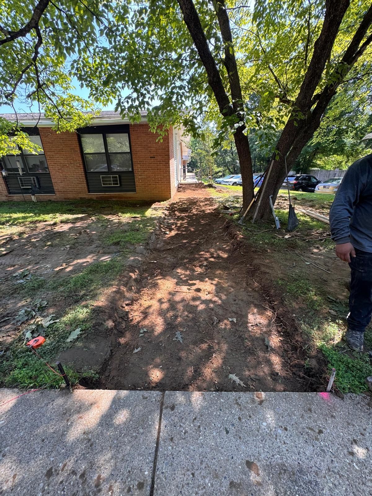 Brick building and trees beside a dirt path, with a person partially visible at right.