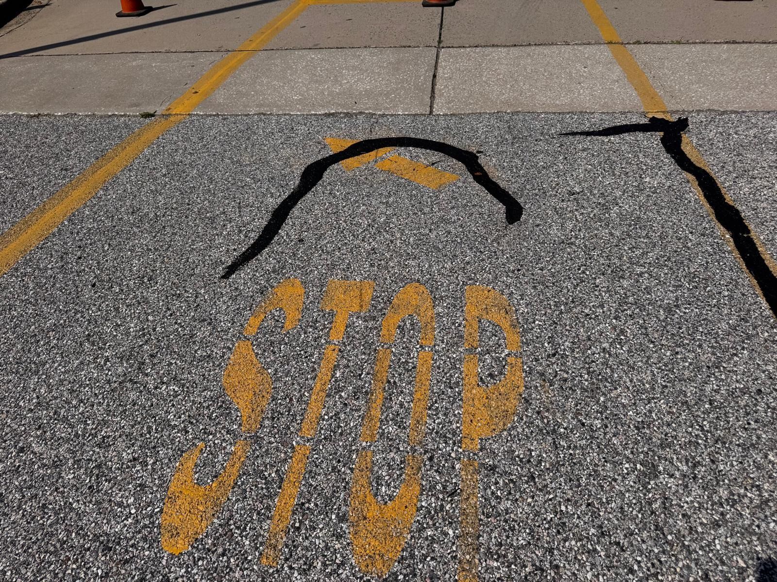 Cracked pavement with a yellow STOP marking and painted curved black lines in a parking lot