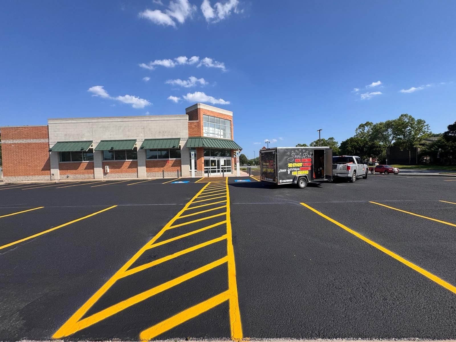 Empty parking lot with yellow striping, a brick storefront, and a truck under a blue sky