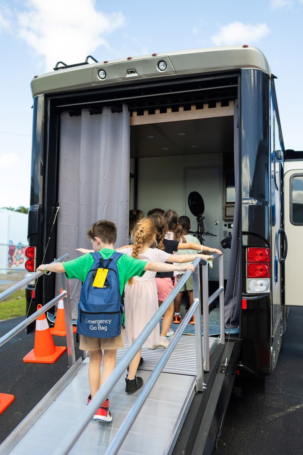 Children line up, arms outstretched, walking up a ramp into a dark vehicle with a curtained opening.
