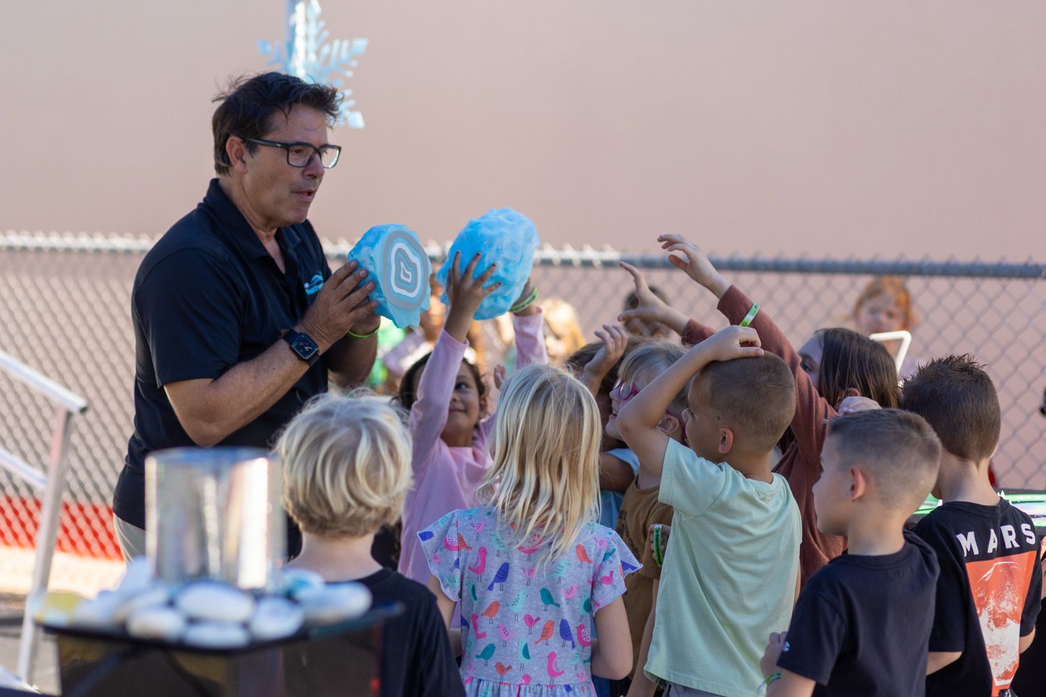 Man demonstrating with blue objects to a group of children outdoors.