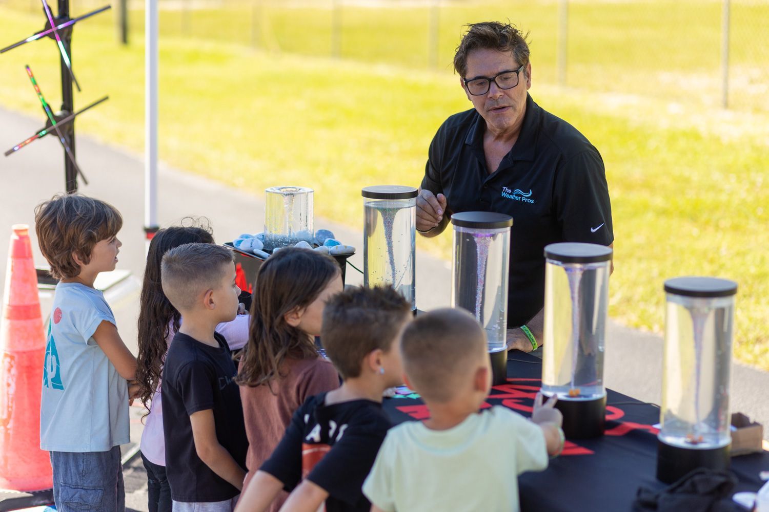 Man demonstrating vortex experiment to a group of children outdoors.