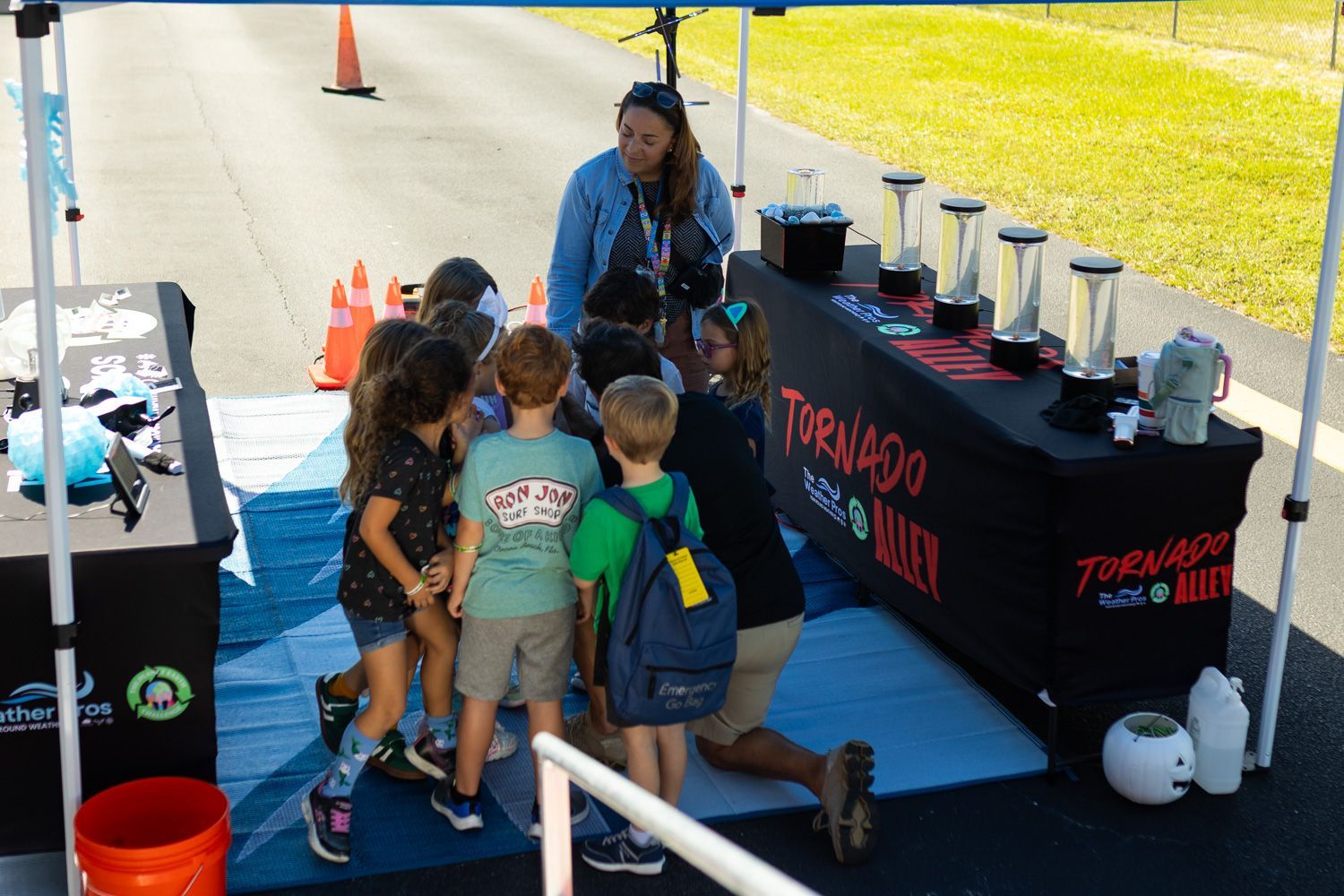 A woman demonstrates a science experiment to a group of children under a tent labeled