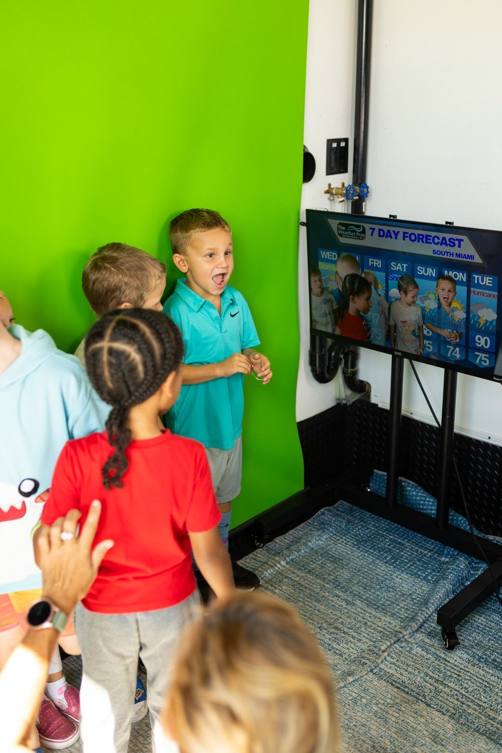 Children looking at a weather forecast on a screen, with a green screen backdrop.