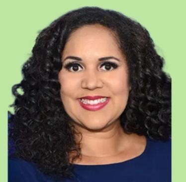 A woman with curly hair is smiling and wearing a blue shirt.