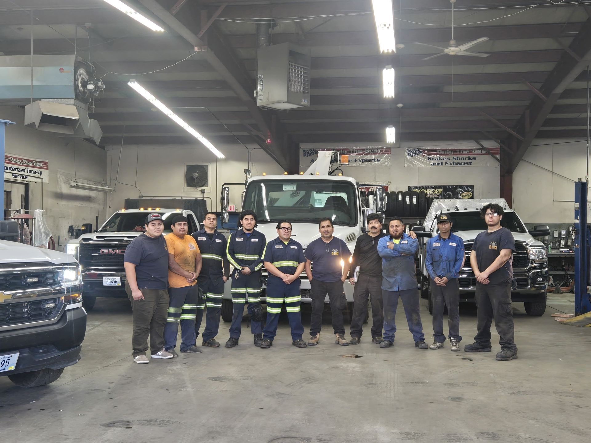 A group of mechanics stands in a garage in front of work trucks.