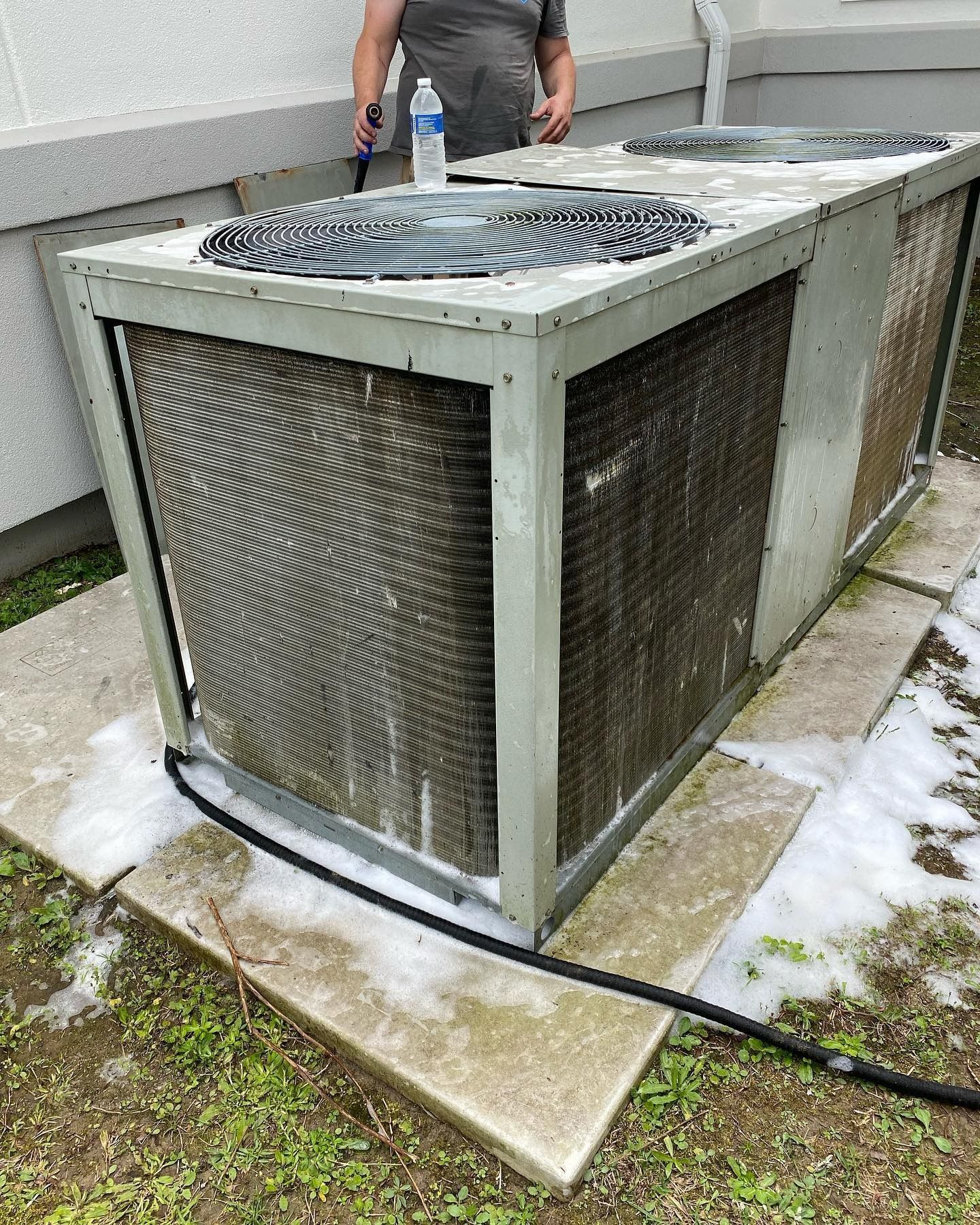 A technician cleans the exterior coils of a large outdoor HVAC unit with a foaming detergent.
