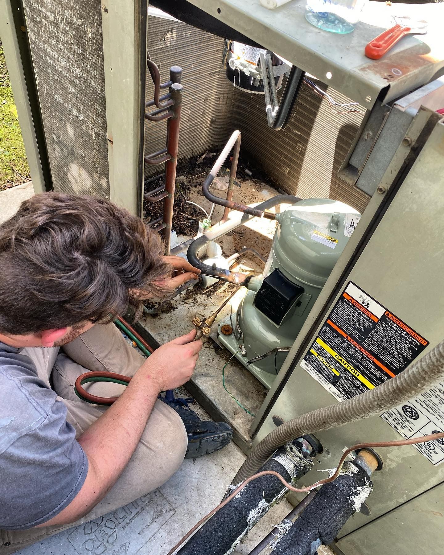 A technician works on the open internal components of an outdoor air conditioning unit.