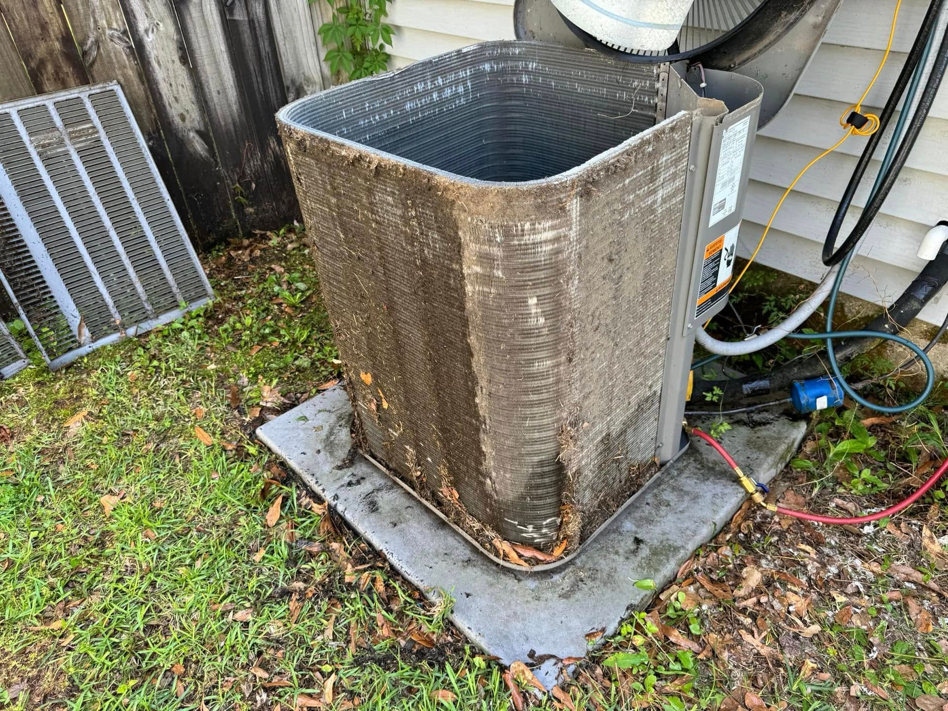 An outdoor air conditioner unit with its protective cage removed, showing exposed, dirty condenser coils.