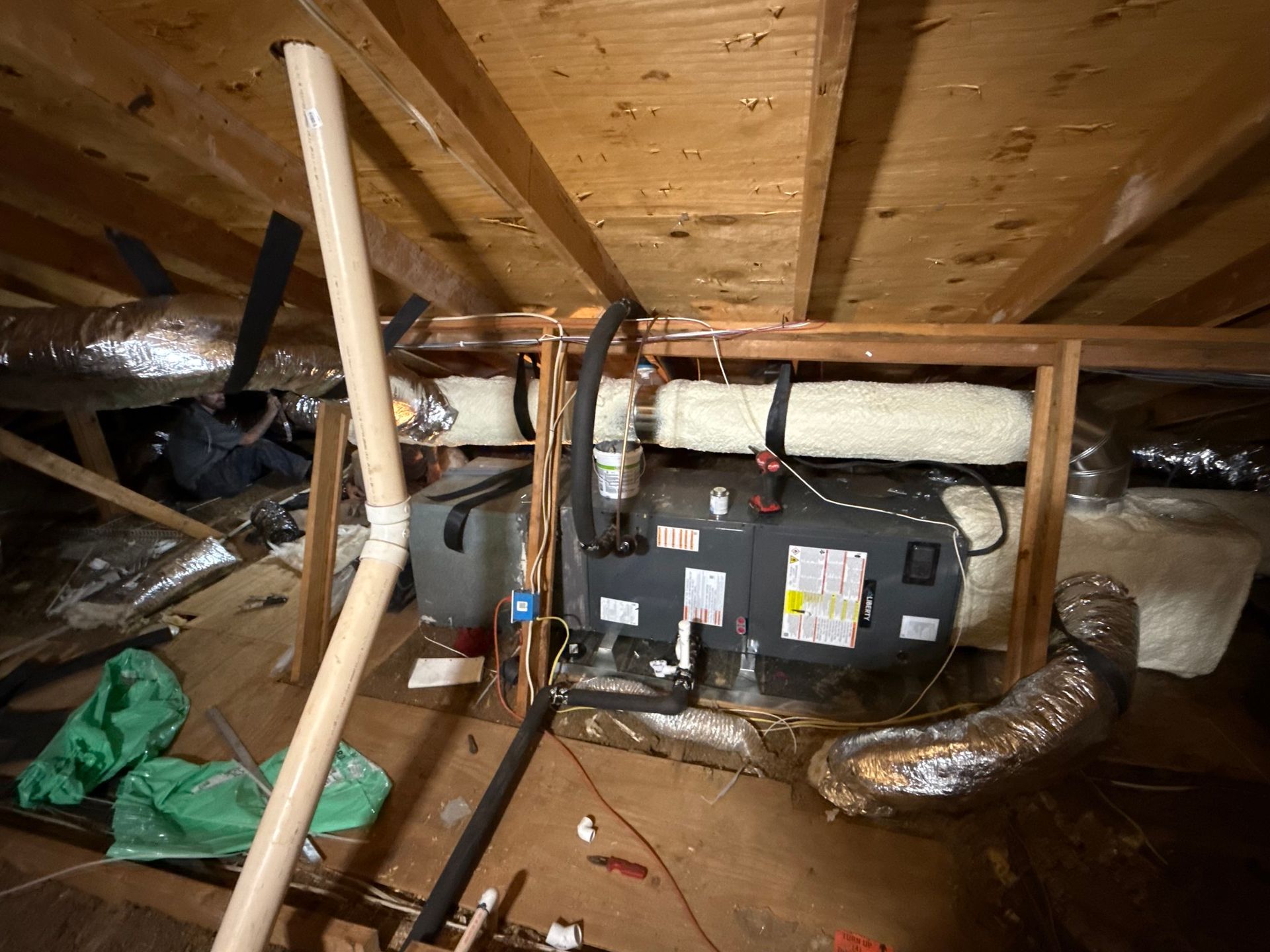 HVAC unit installed in an attic crawlspace, featuring silver and insulated ductwork beneath wooden roof rafters.