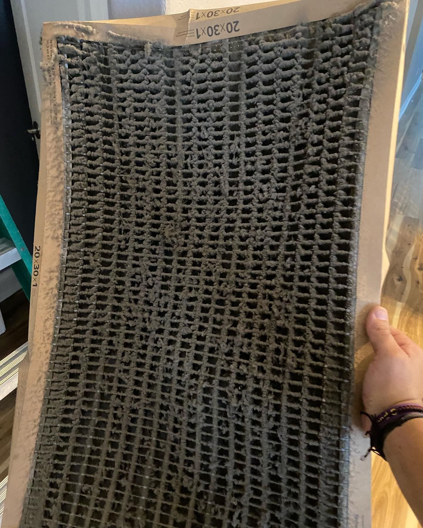 A hand holds a heavily dust-clogged HVAC air filter, showing significant accumulation of gray debris.