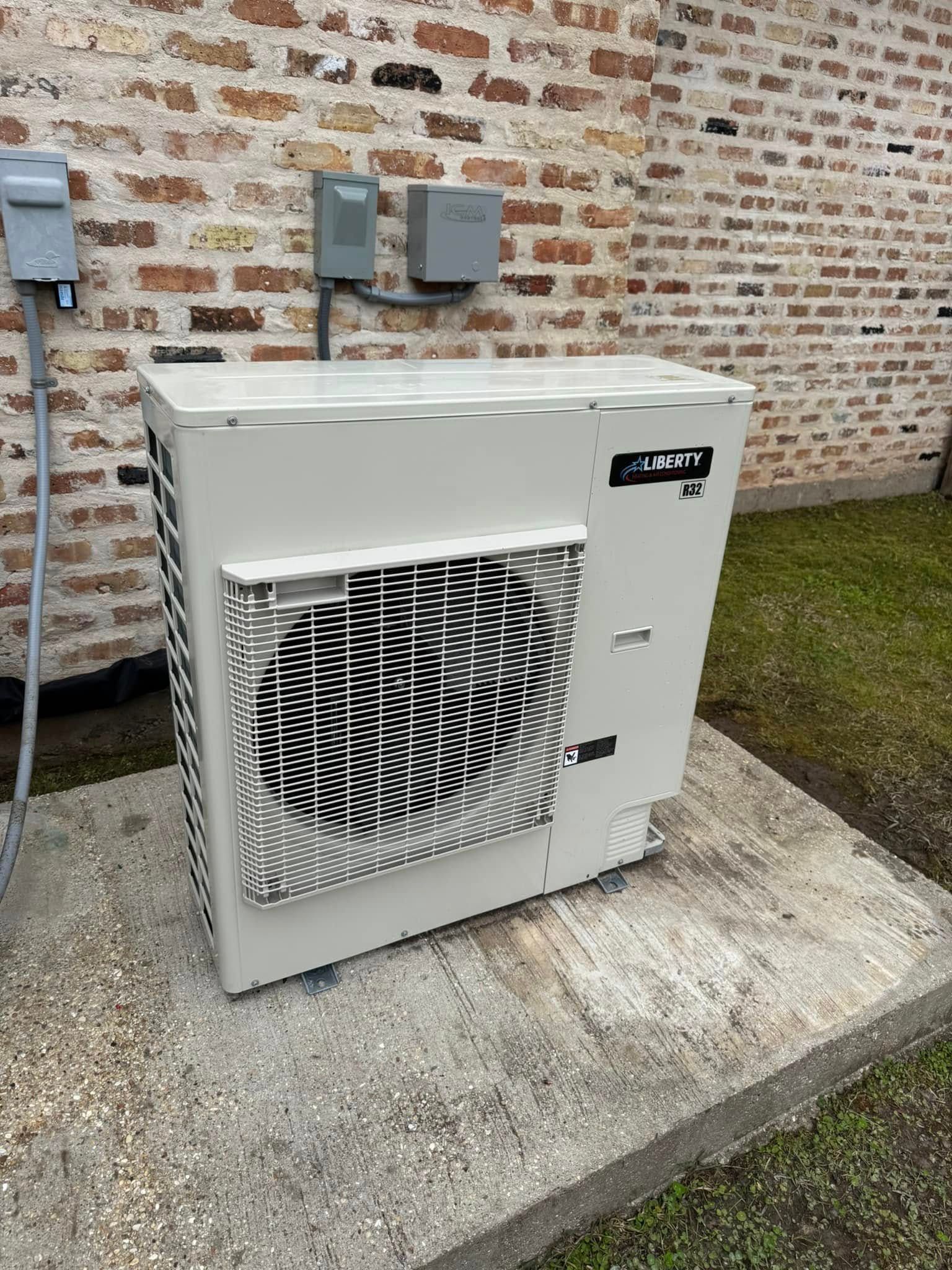 A light-colored outdoor HVAC condenser unit sits on a concrete pad against a brick wall.