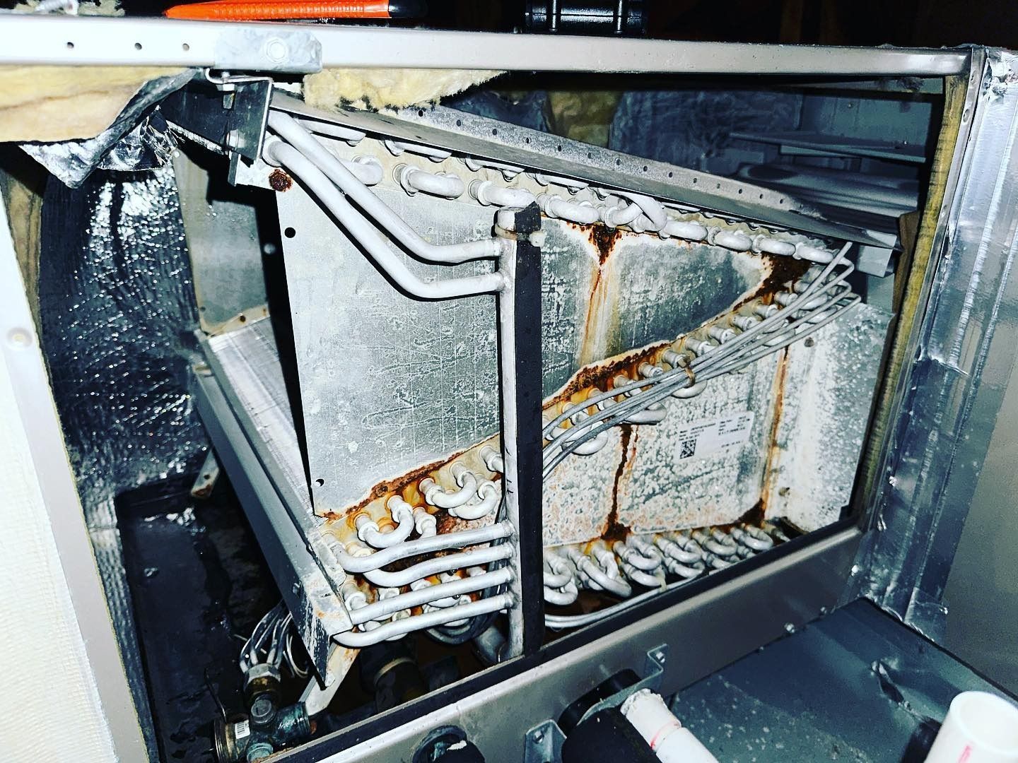 The interior of an HVAC air handler unit showing a triangular A-coil evaporator with visible rust and corrosion.
