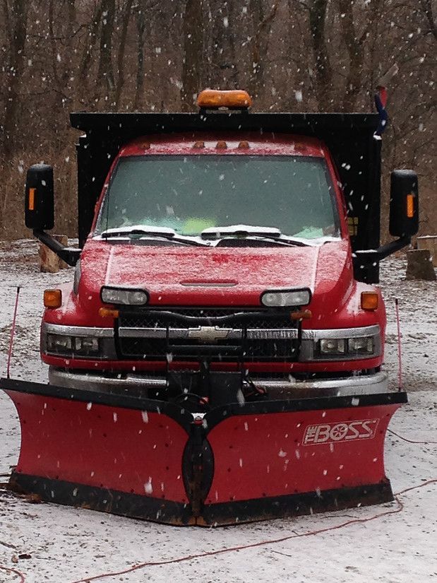 Red snowplow truck with front blade in a snowy wooded area