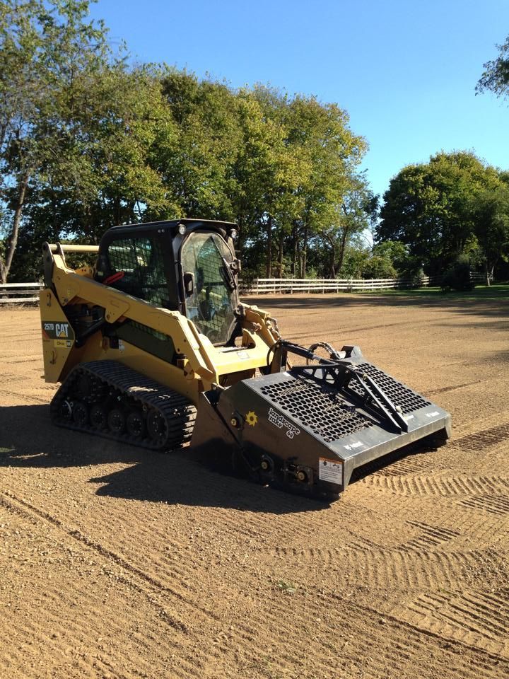 Yellow compact track loader on a dirt lot with trees in the background