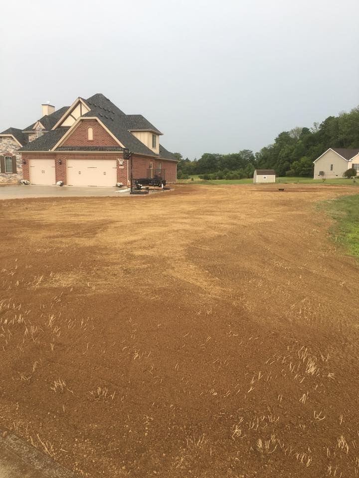 Large brick house with a driveway on a dirt lot, with another house in the distance.