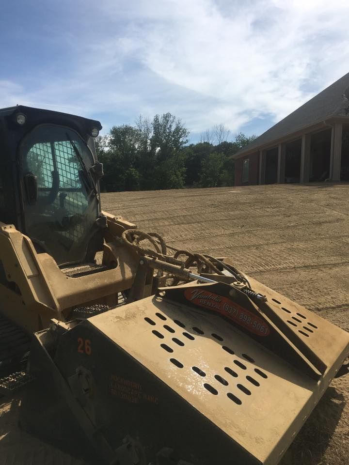Construction skid steer with a brush cutter attachment parked outdoors beside a building.