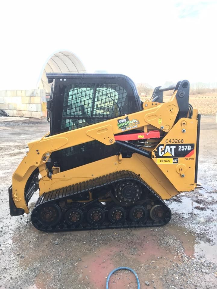 Yellow CAT skid steer loader on tracks parked outdoors on wet ground.