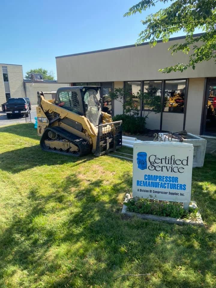 Skid steer parked on a lawn outside a building with a Certified Services sign in front