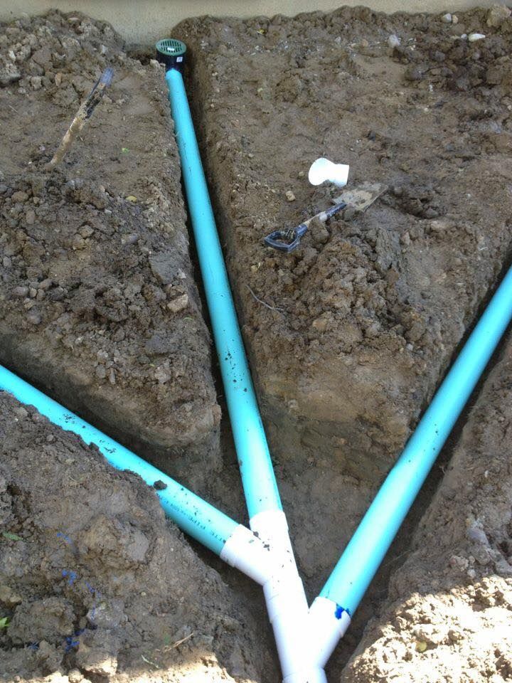 Blue PVC pipes joined in a Y-shape emerging from muddy soil